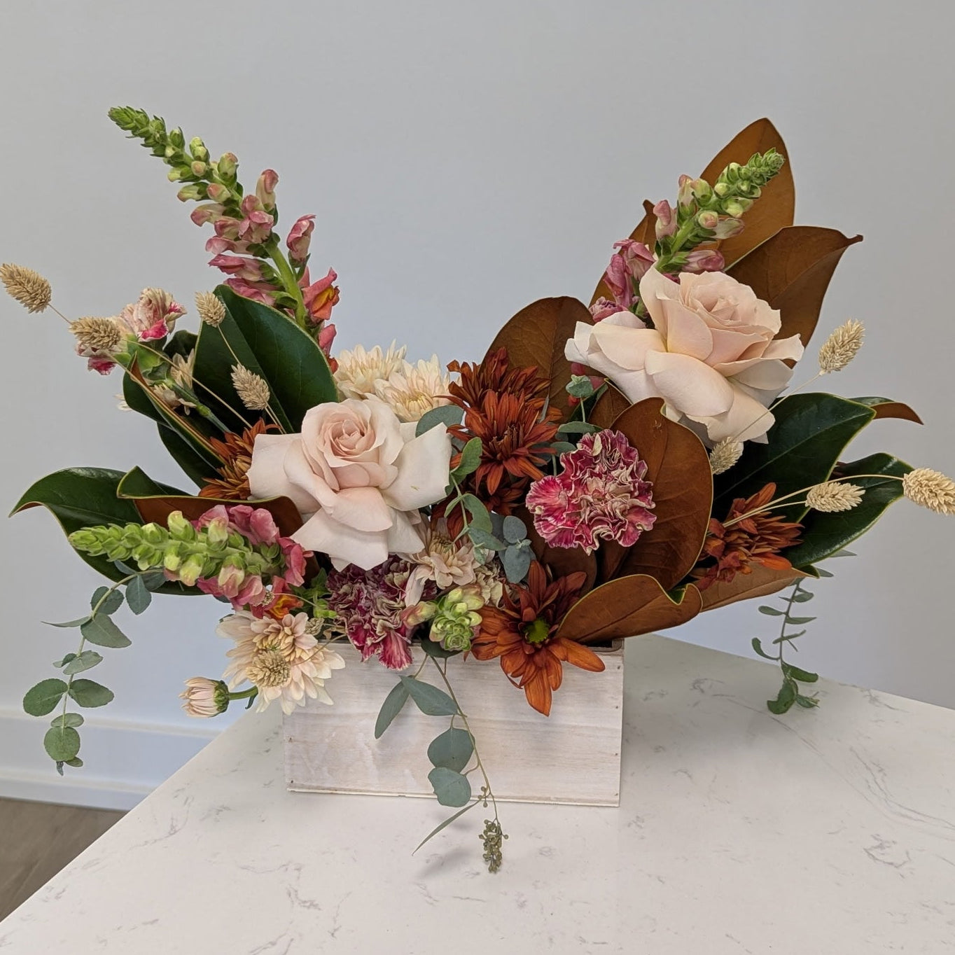 Floral arrangement with autumnal colors on a marble surface against a light gray wall.