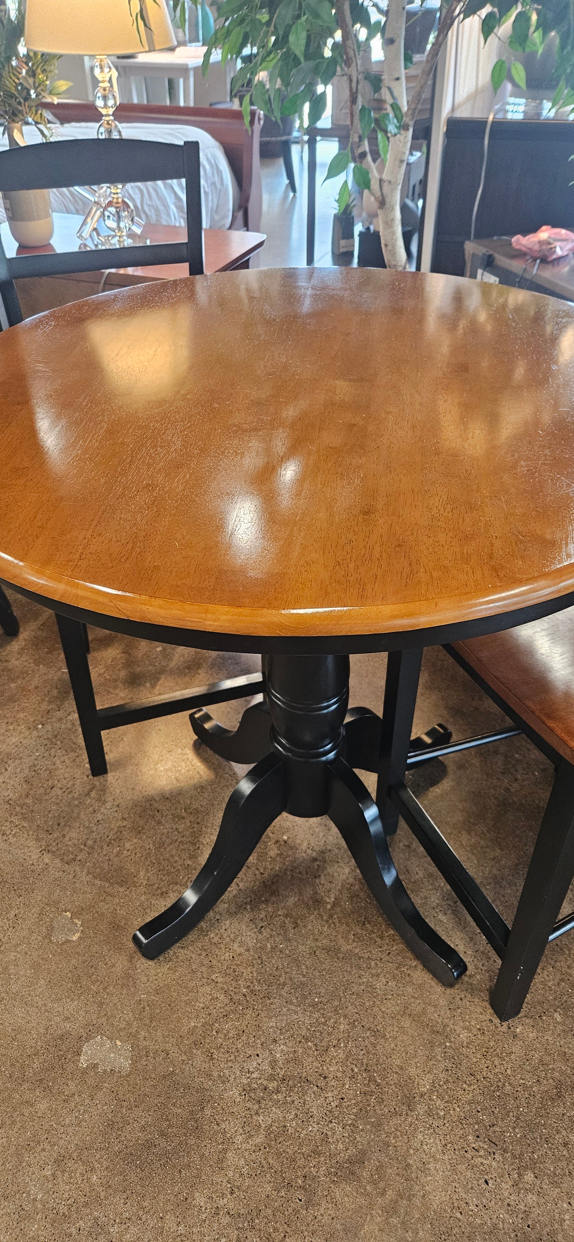 A round wooden table with a glossy brown finish and a black metal pedestal base.