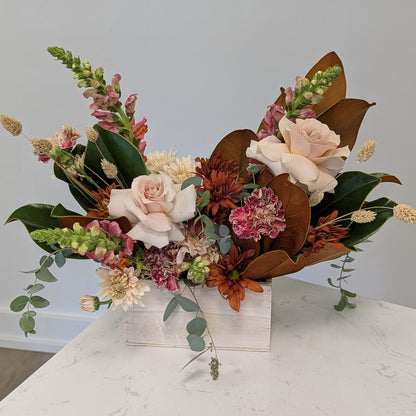 Floral arrangement with autumnal colors on a marble surface against a light gray wall.