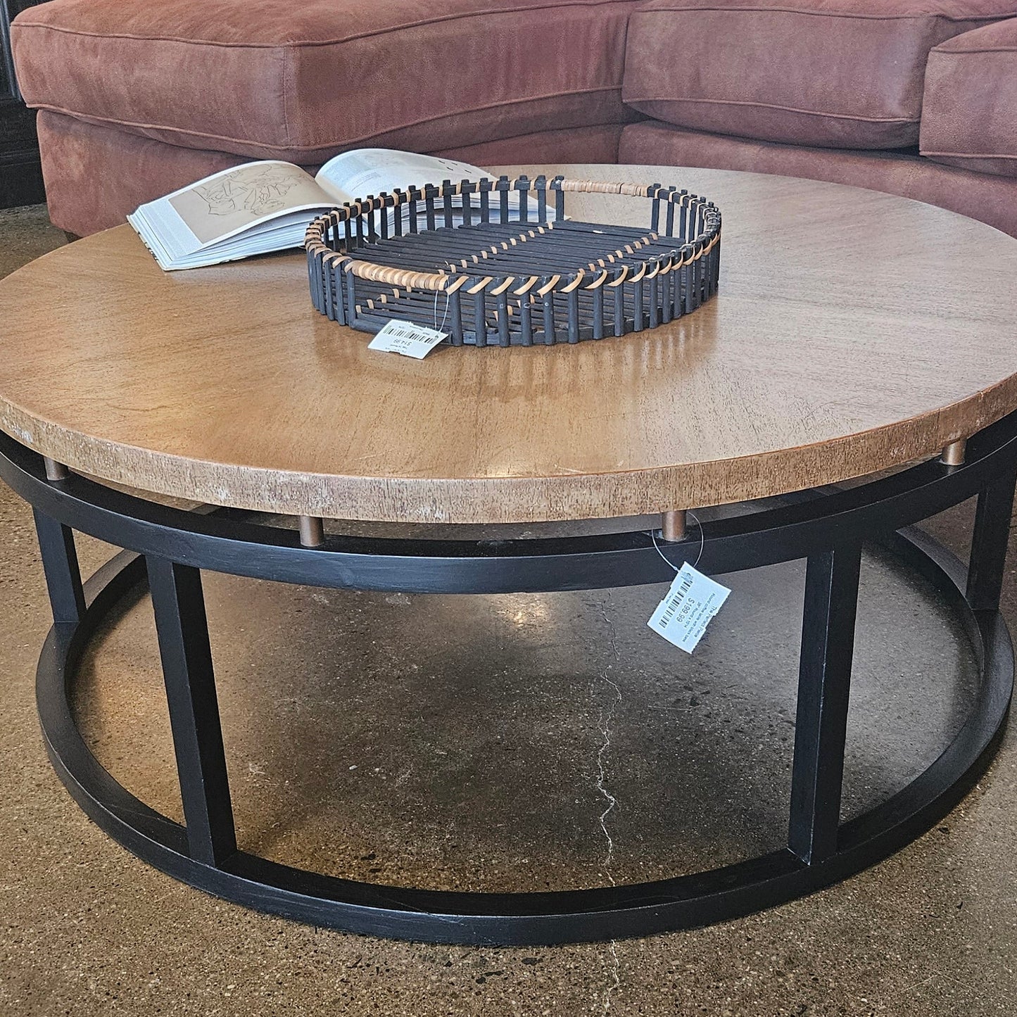 A round coffee table with a light wood top and a black metal circular frame base.
