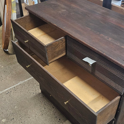 A dark brown wooden dresser with three open drawers showing light wood interiors.